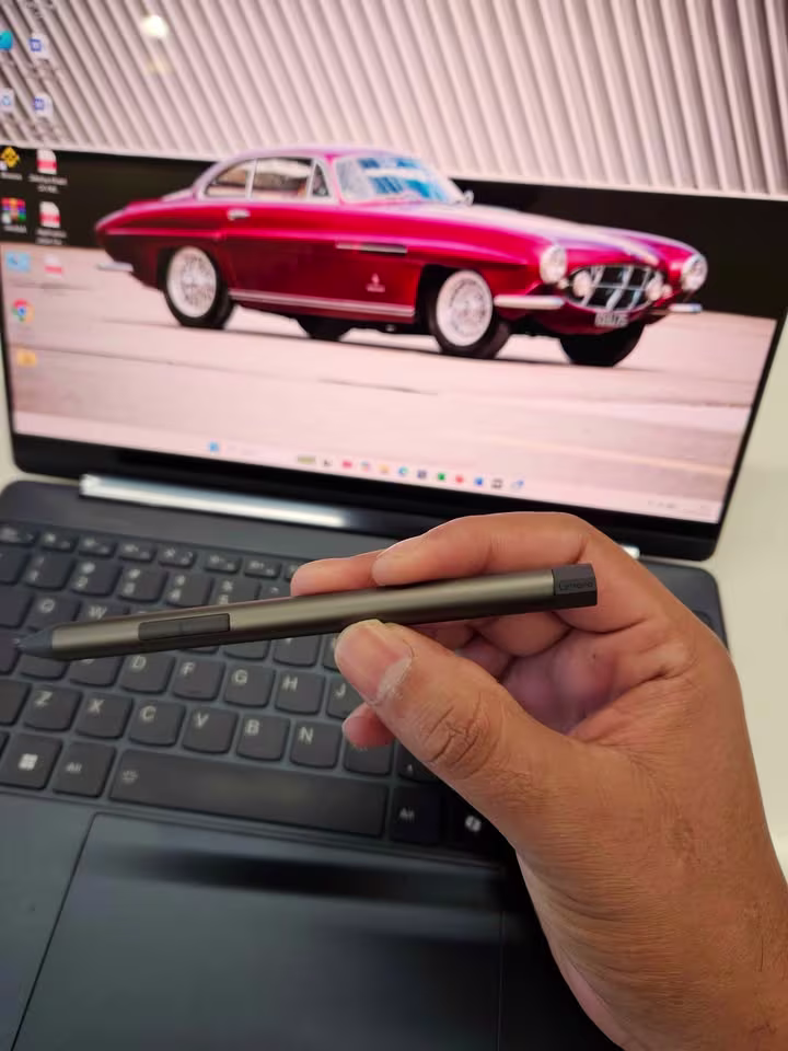 Close-up of Lenovo Yoga Slim 9 stylus pen with metallic gray finish and side button, held in hand for size and grip comparison